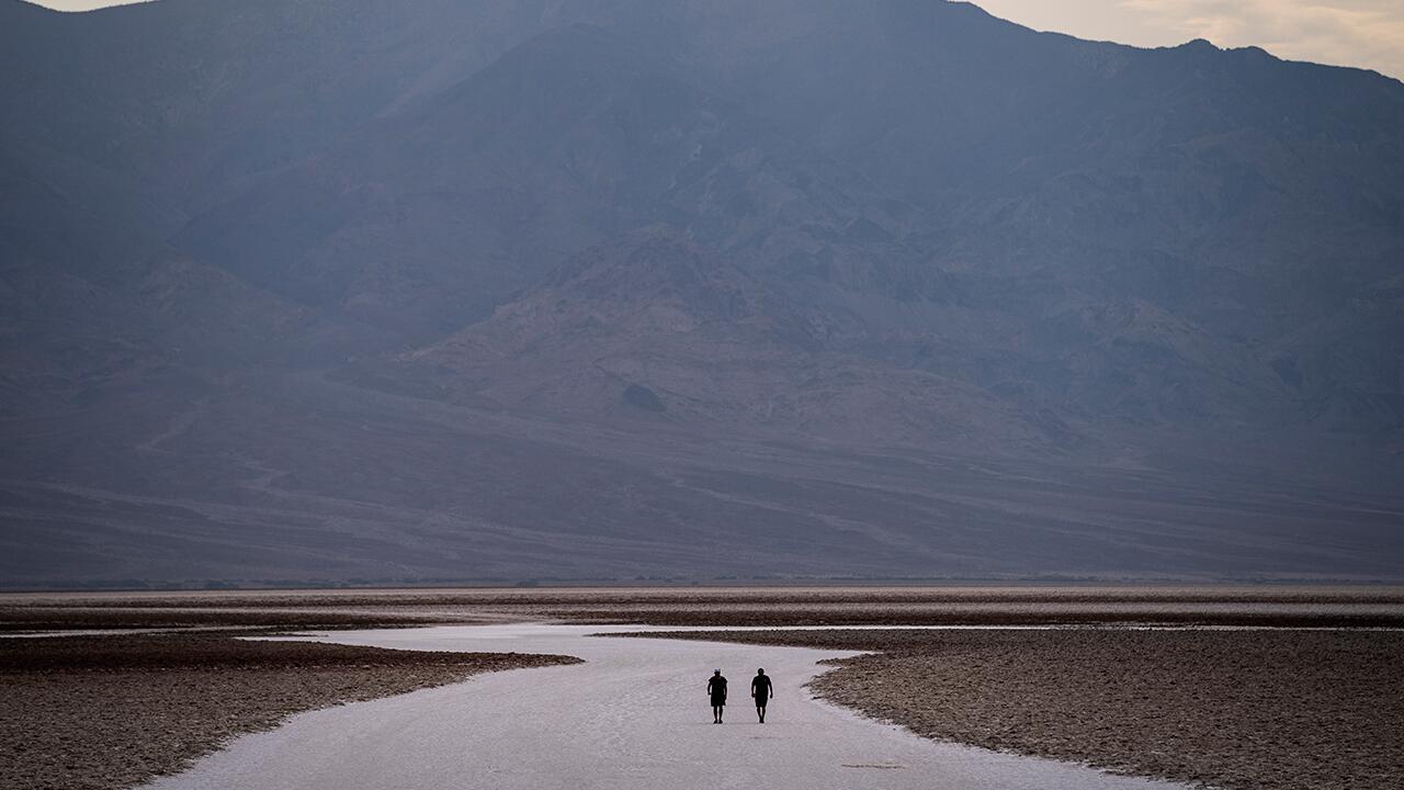 USA, Death Valley National Park: Menschen spazieren auf Salzebenen im Badwater Basin. Der Klimawandel könnte nach Ansicht von Experten im schlimmsten Fall zum Aussterben der Menschheit führen.