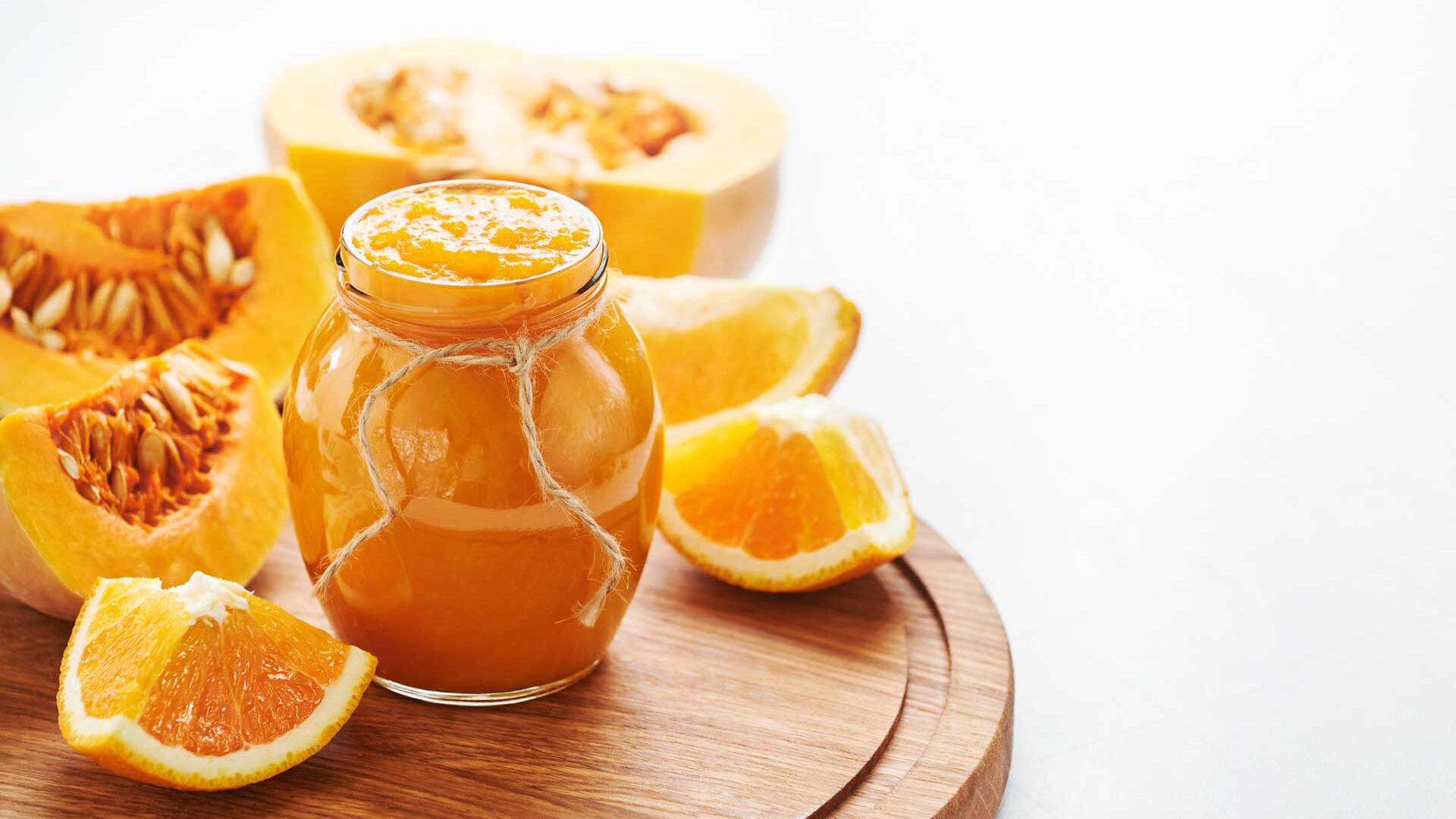 Ein Glas Kürbismarmelade auf einem Brett, mit Kürbisspalten im Hintergrund. Ein Glas Kürbismarmelade auf einem Brett, mit Kürbisspalten im Hintergrund.