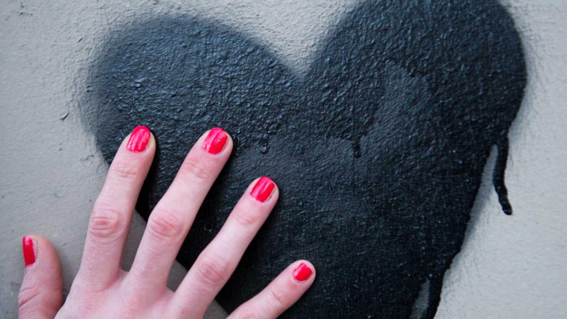 Frauenhand berührt ein auf die Wand gesprühtes Herz Frauenhand berührt ein auf die Wand gesprühtes Herz
