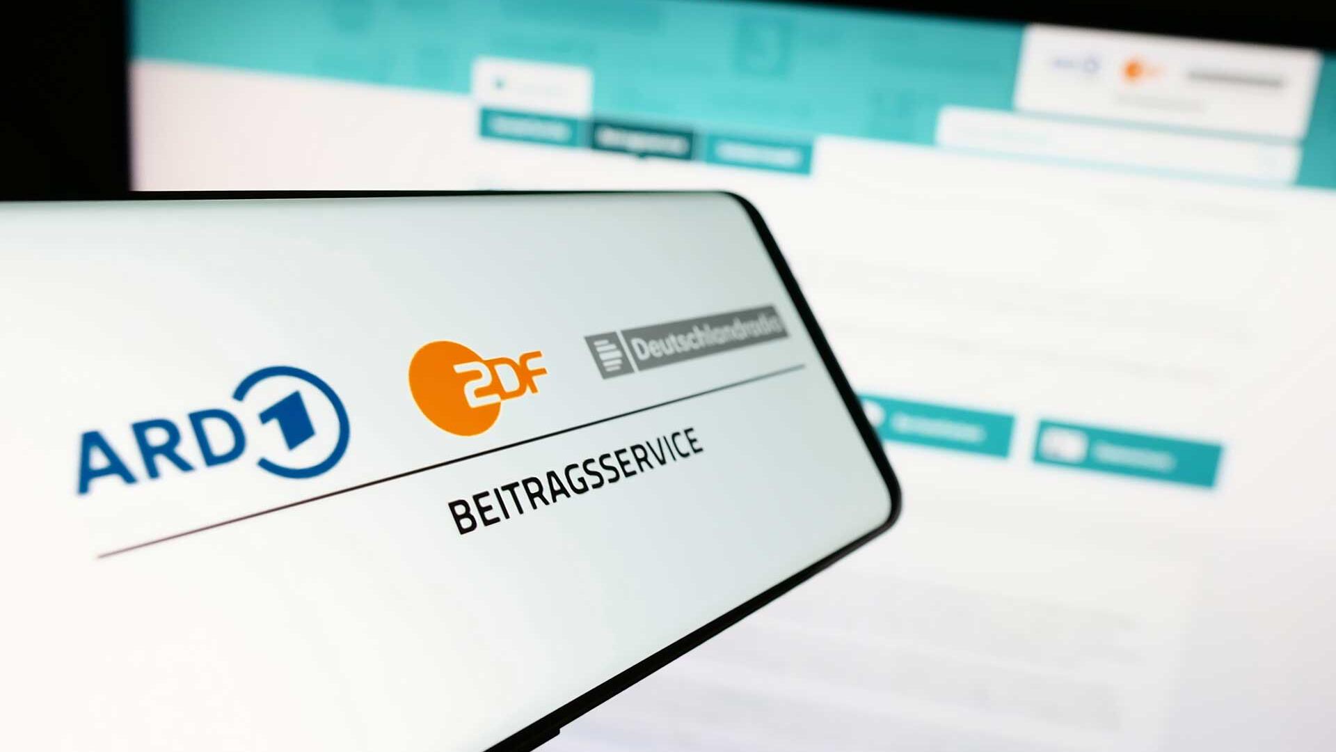 Handy vor Bildschirm, auf dem Display steht "Beitragsservice"