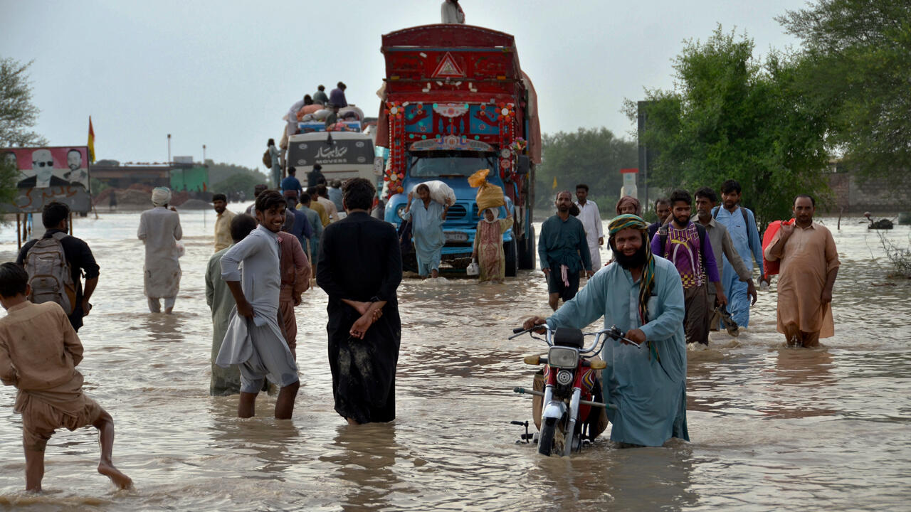 akistan, Nasirabad: Menschen gehen durch eine Straße, die durch schwere Monsunregenfälle überschwemmt wurde. 