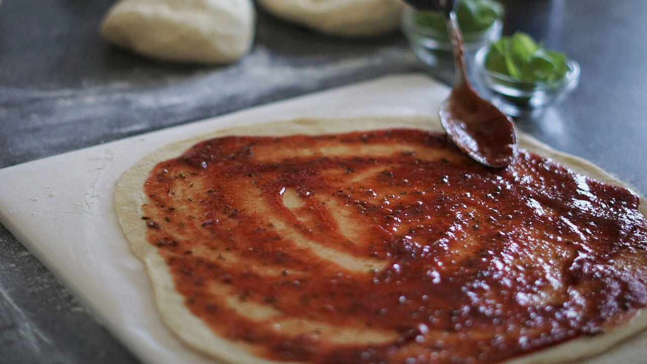 Den Pizzateig kreisförmig mit Tomatensoße bestreichen. Den Pizzateig kreisförmig mit Tomatensoße bestreichen.